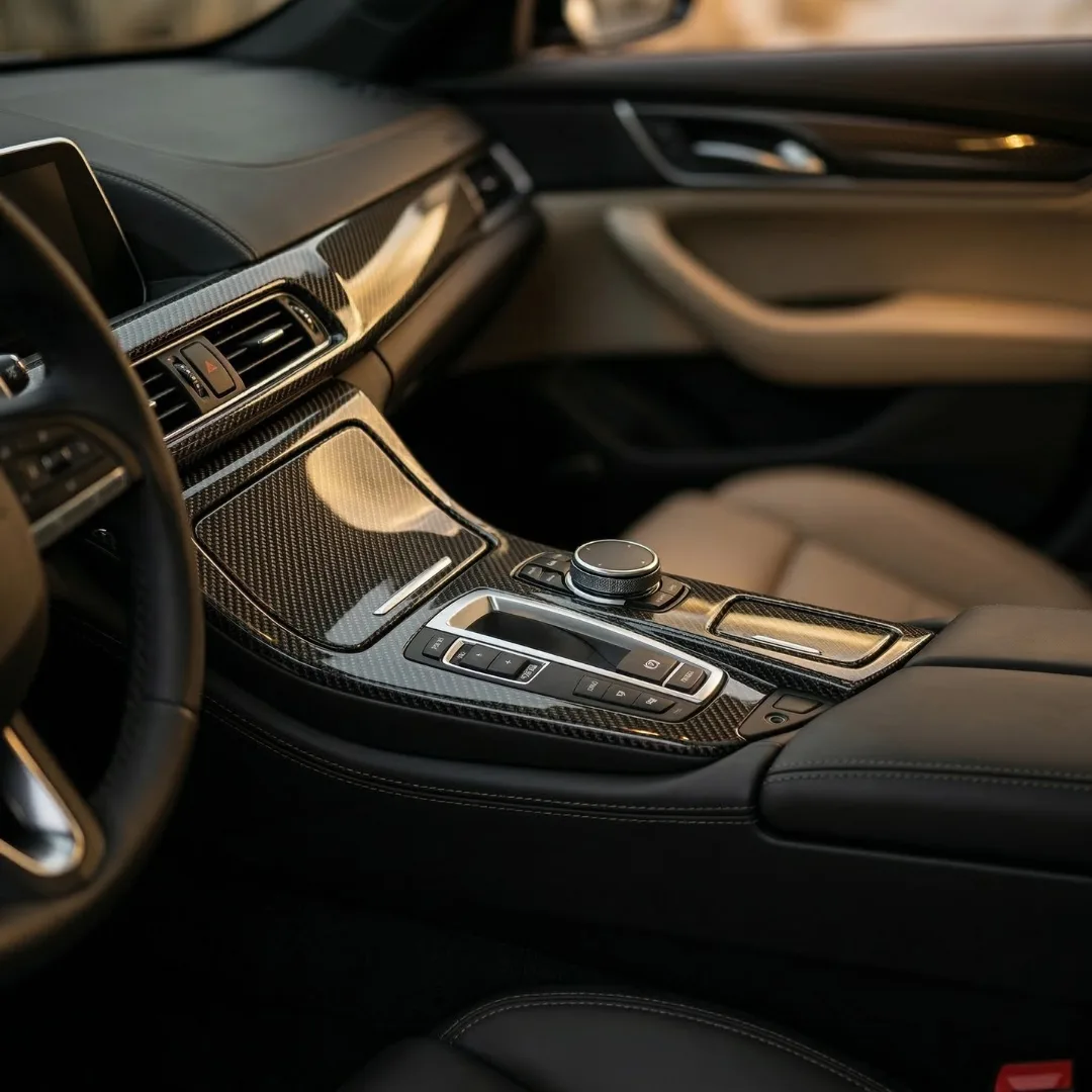 Panel trim carbon fiber DEMIN terpasang di dalam mobil mewah, memantulkan cahaya ambient lembut di antara permukaan kulit hitam