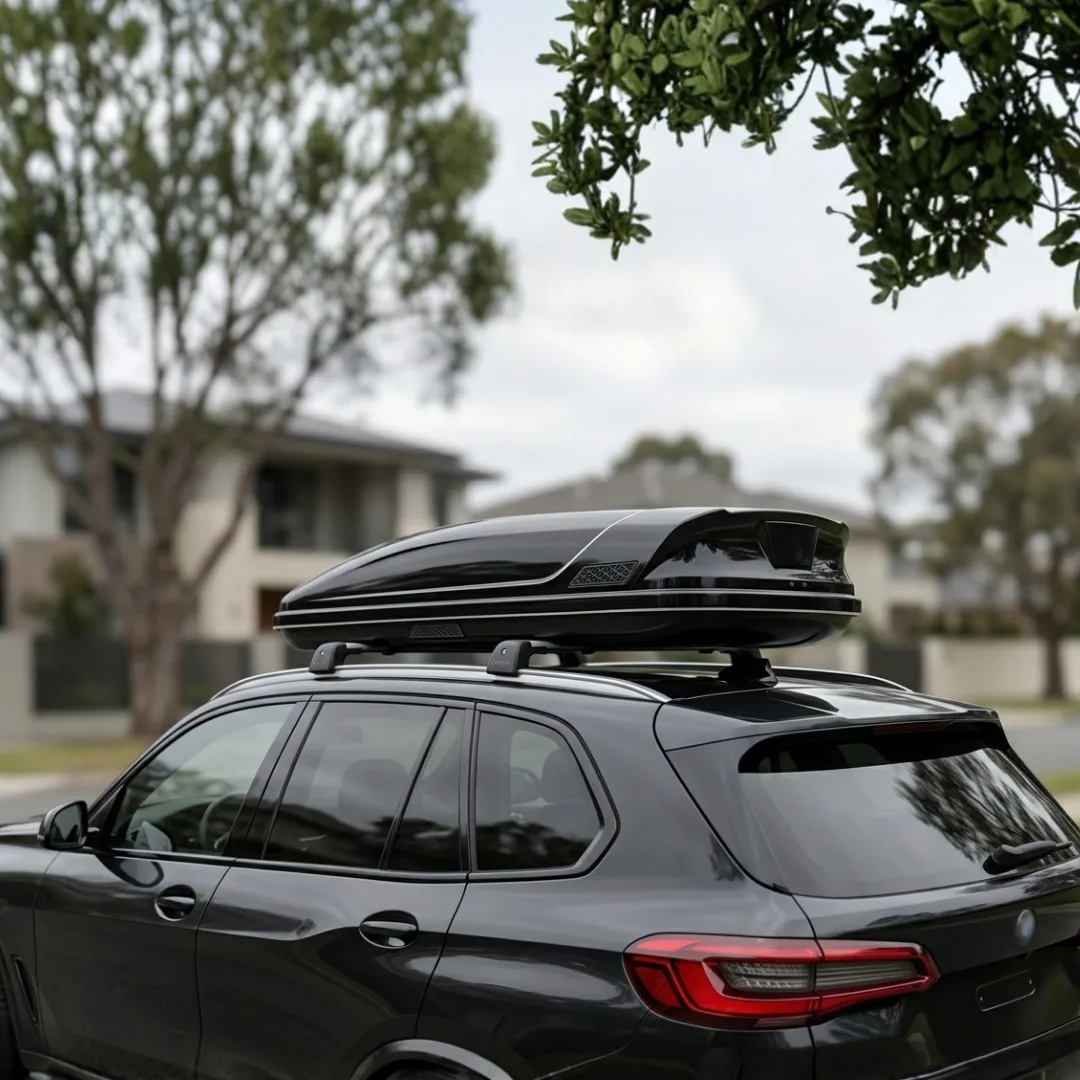 Roof box gloss black DEMIN terpasang sempurna di atas SUV mewah, mengikuti lekukan roofline dengan presisi, difoto dari sudut tiga perempat belakang